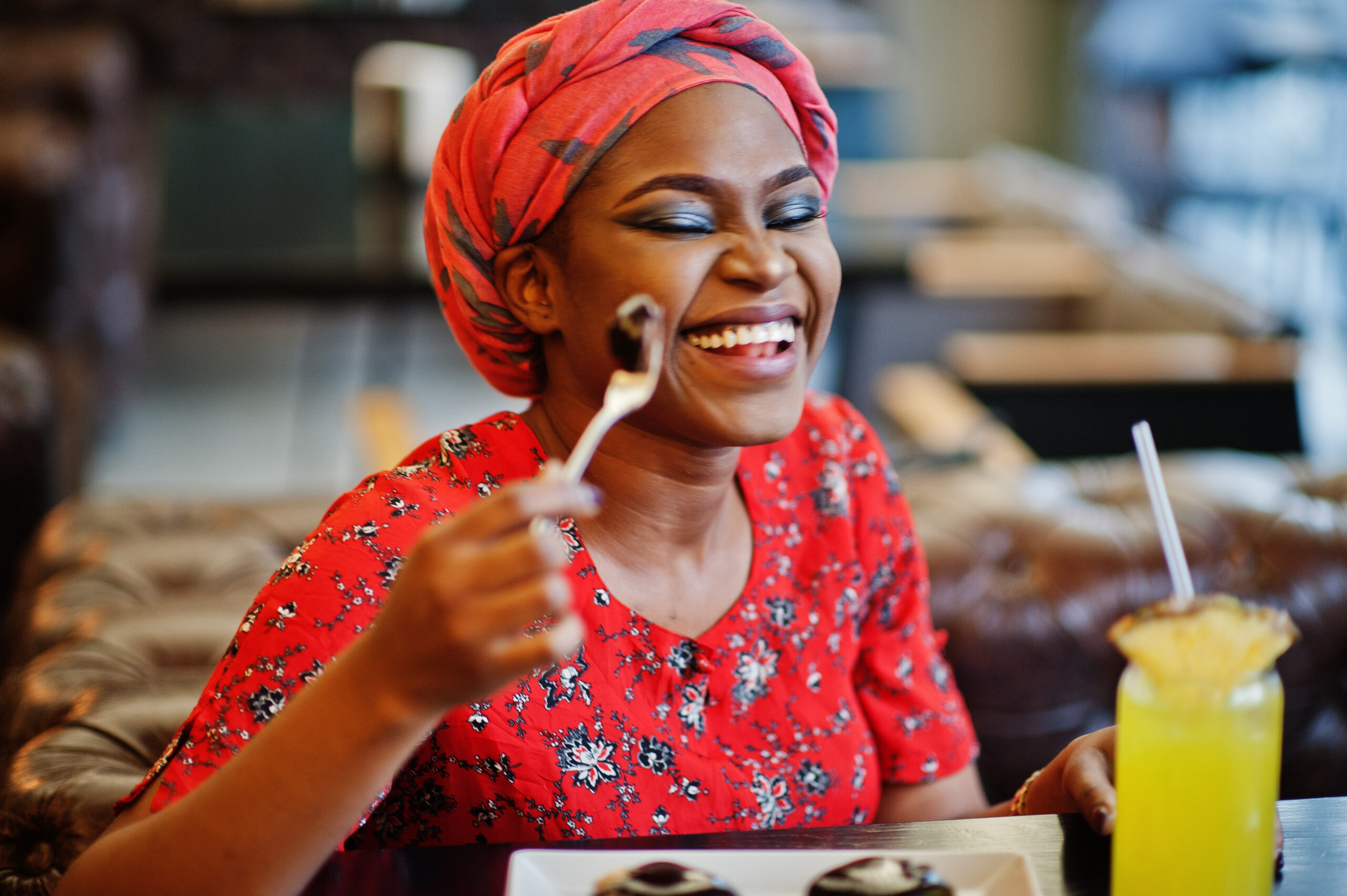 Stylish african woman in red shirt and hat posed indoor cafe, eat chocolate dessert cakes.